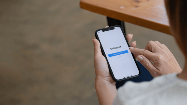 Mulher de camisa branca segurando celular aberto na tela de login do Instagram