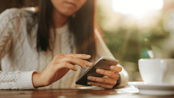 Mulher de branco com celular na mão descobrindo o que significa contas alcançadas no Instagram