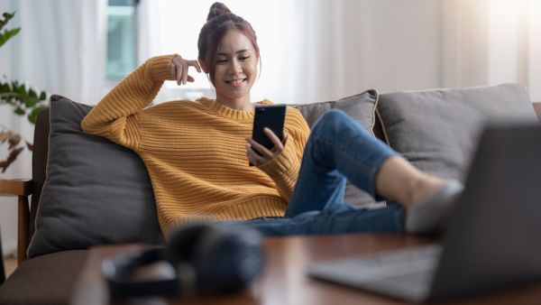 Mulher com blusa amarela feliz olhando para tela do celular