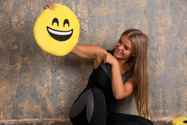 Mulher sorrindo tirando foto apontando para almofada de emoji sorrindo